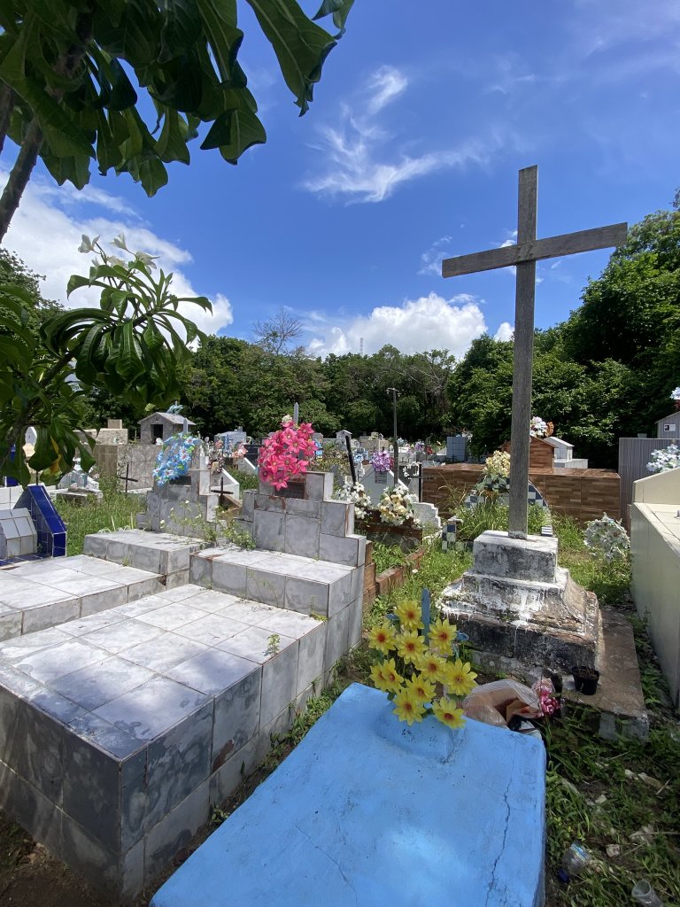 Steingräber mit bunten Kunstblumen, Holzkreuz und einem kleinen steinernen Mausoleum vor der Kirche Nossa Senhora da Guia in Lucena