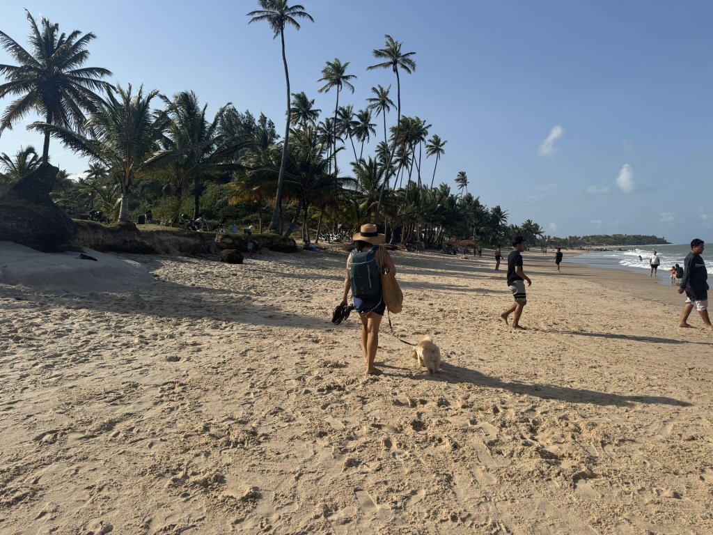 Lili und Schleckie gehen am Strand von Tabatinga II entlang, die Sonne steht tief, Palmen und goldener Sand im Abendlicht.