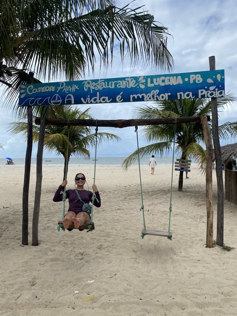 Frau sitzt nach dem Mittagessen auf einer Schaukel am Praia de Lucena, im Hintergrund das Meer und sanfte Wellen