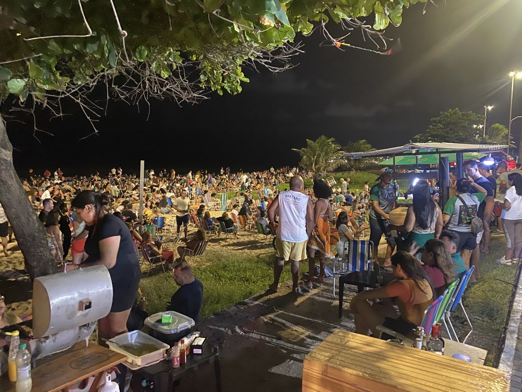 Menschen sitzen mit Strandstühlen am Strand von João Pessoa, hören Live-Musik und genießen Essen und Getränke bei Nacht