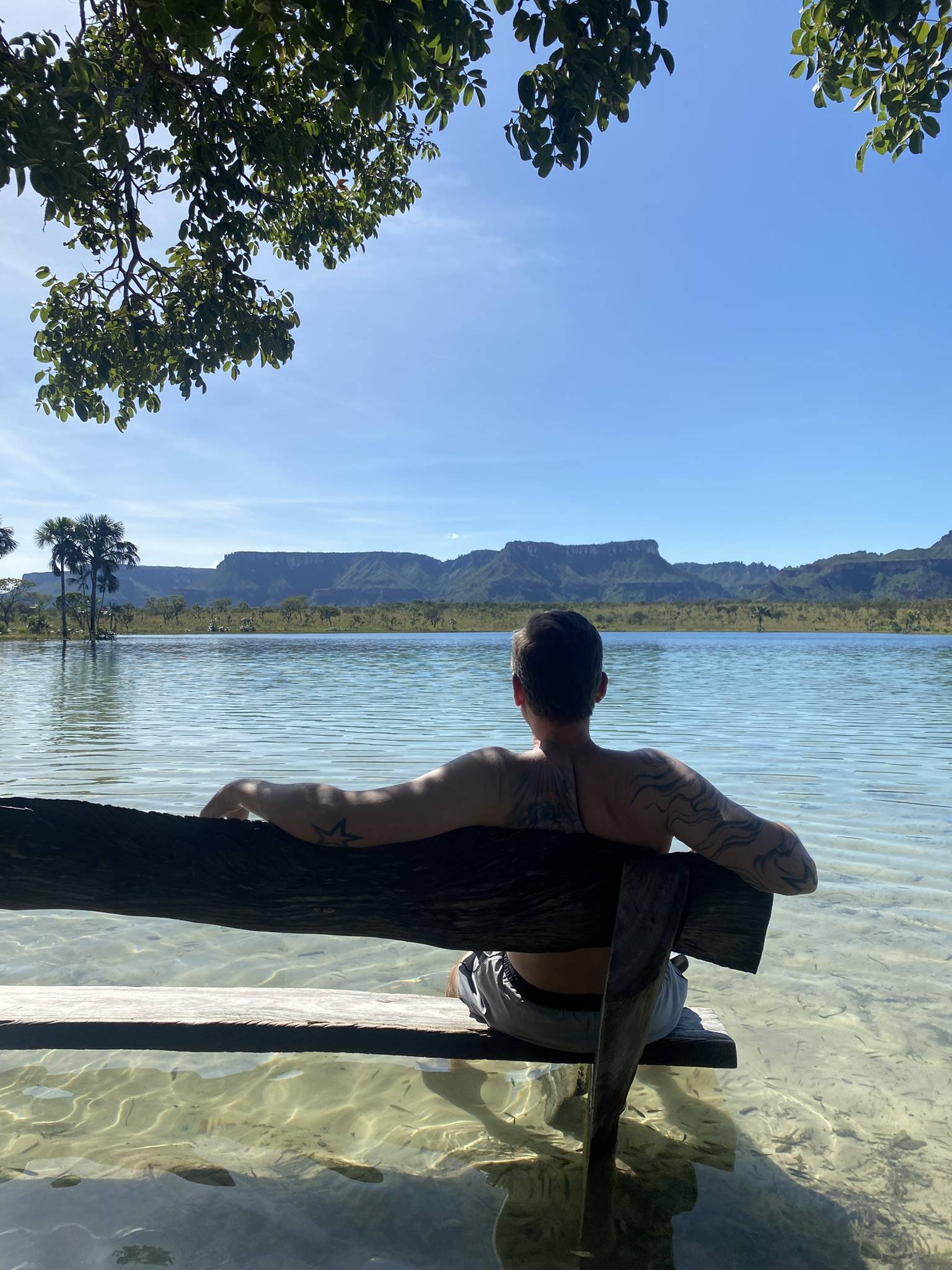 Lagoa da Serra bei Rio da Conceição – Person sitzt auf einer Holzbank im Wasser und blickt auf die Bergkette
