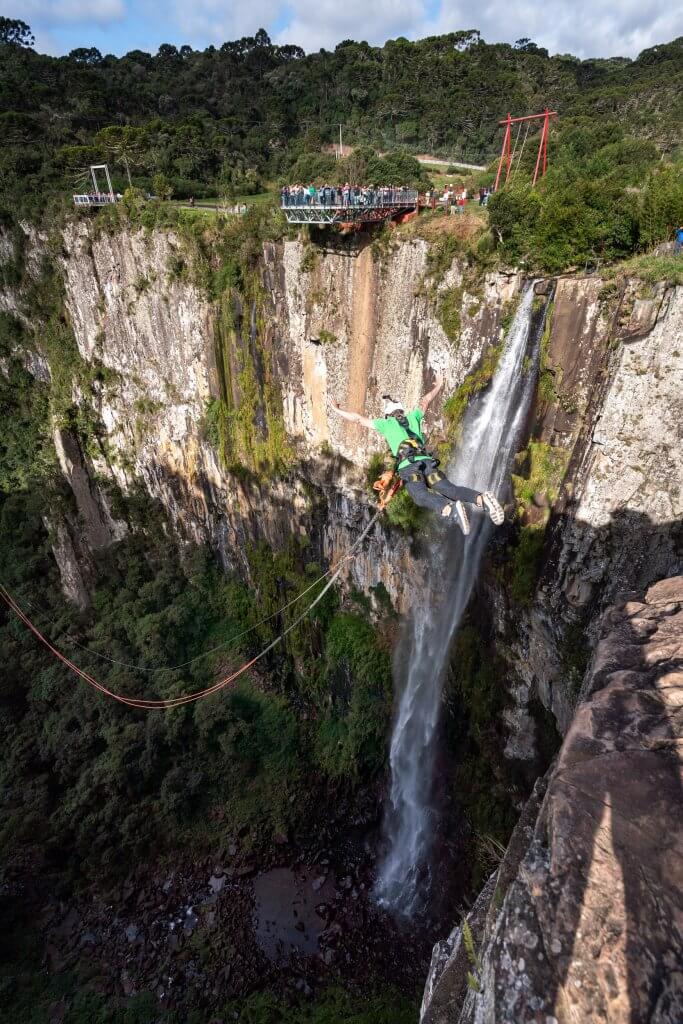 Sven springt beim Salto de Pêndulo in die Schlucht, im Hintergrund der Wasserfall in Urubici